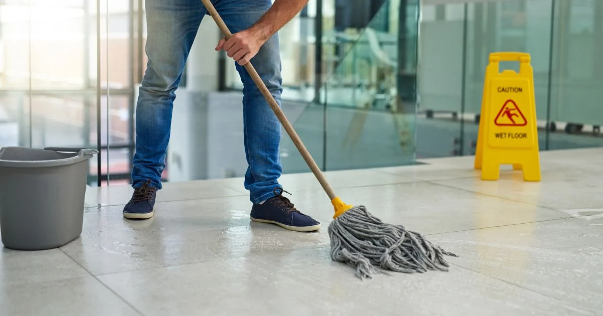 Janitor mopping wet floor with caution sign nearby